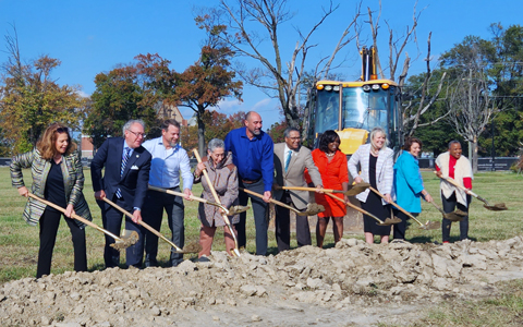 Ten individuals move dirt with shovels to celebrate the project’s groundbreaking.