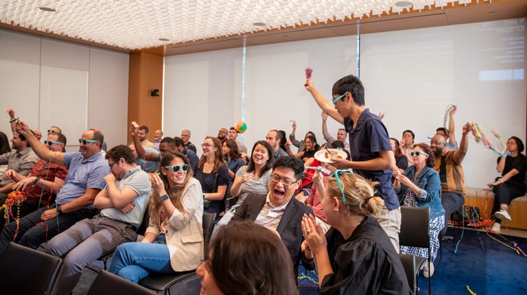 Employees celebrate Milestones with sunglasses, beach balls, and noisemakers in a conference room.
