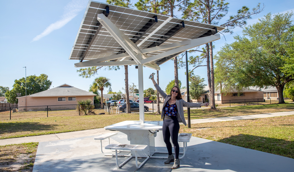 Katie stands under a park picnic table with a solar panel awning and wi-fi connectivity.
