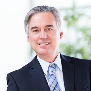 David Wilcock wearing a blue suit and tie. 