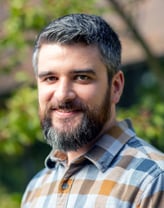 Andrew Vitale smiling outside in a checkered shirt.