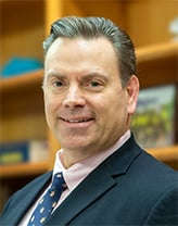 Brian Perry in the office wearing a dark blue suit and tie.