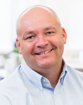 Chris Lovett smiling outside in a white shirt.