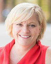 Heidi Richards smiling in an orange dress. 