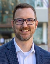 Jay Jenkins smiling in a navy-blue blazer.