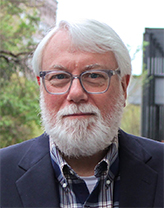 John shown outside wearing glasses, blue jacket.