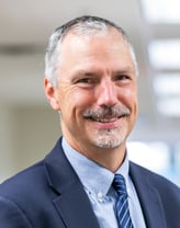 Joe Balskus smiling in a navy suit and navy tie.