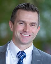 Mark Grocki smiling in a white shirt, tie, and gray sport jacket. 