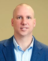 Nick Fetzer smiling in a navy blue blazer and blue checkered shirt.