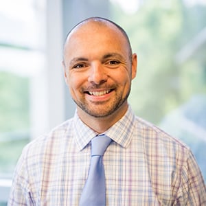 Frank Gross smiles at the camera wearing a striped button up shirt.