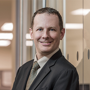 Tom Velleca in a dark brown suit and brown checkered tie