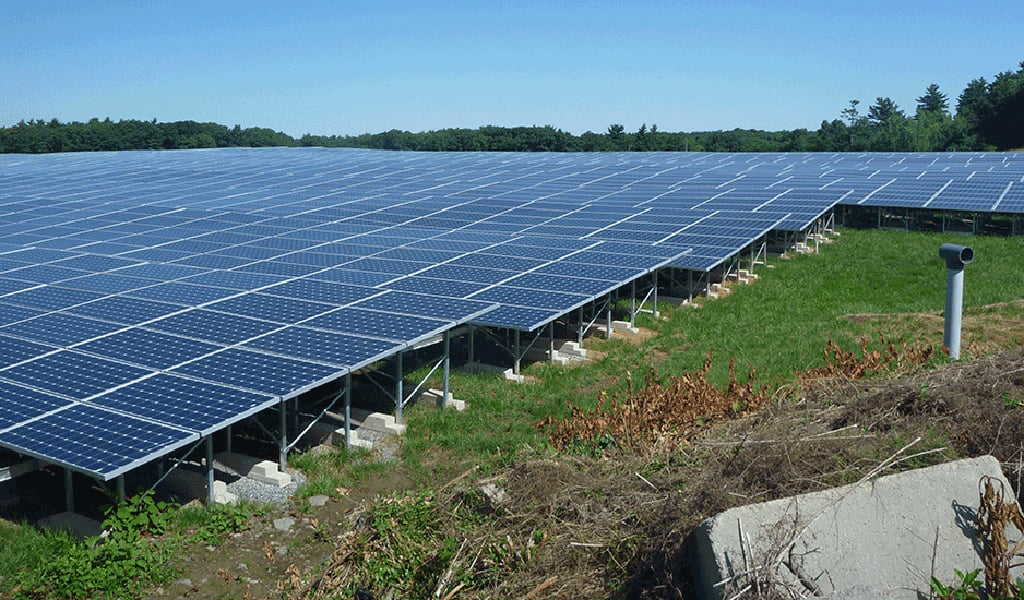 Rows of solar panels line a grassy field on a closed landfill in Canton, Massachusetts.