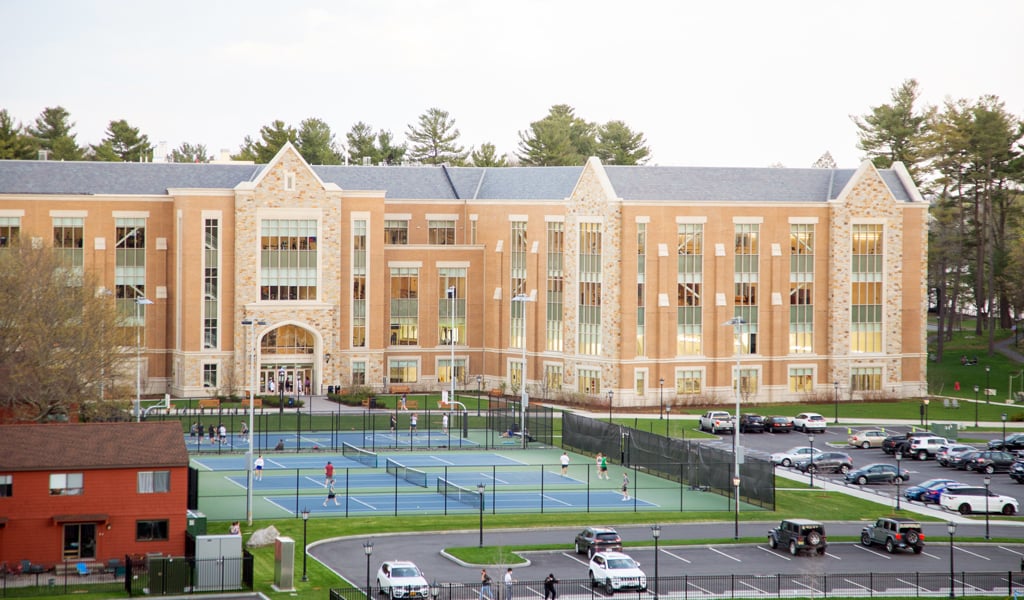 People playing tennis at the outdoor tennis courts with the Margot Connell Recreation Center in the background.