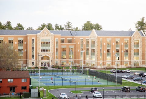 People playing tennis at the outdoor tennis courts with the Margot Connell Recreation Center in the background.