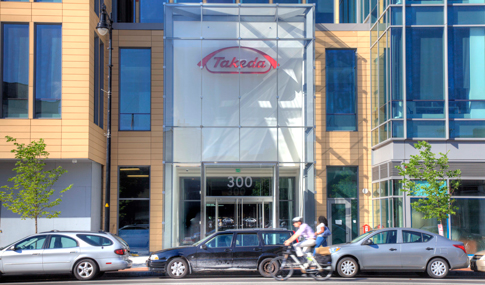 A cyclist rides past the entry to Takeda’s building at 300 Massachusetts Avenue in Cambridge.