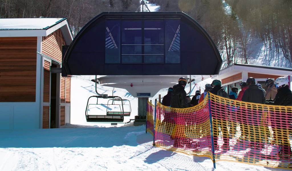 View of the high speed lift in the wintertime with skiers lined up in the queue to get on the list. 