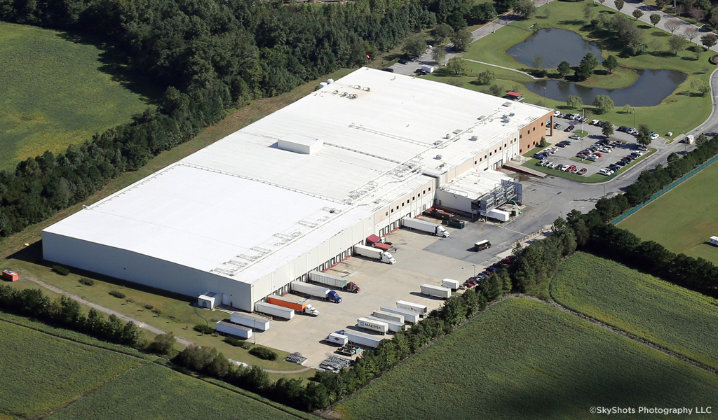 Aerial view of white cold storage facility with trucks parked outside.