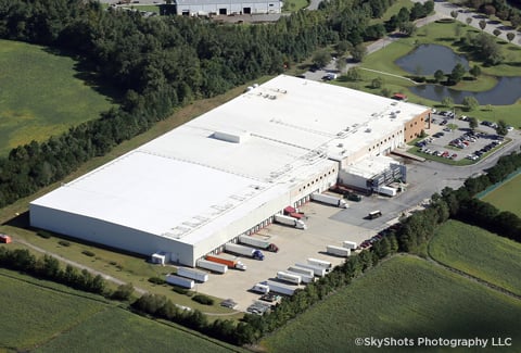 Aerial view of white cold storage facility with trucks parked outside.