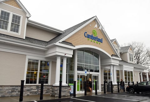 A modern Cumberland Farm store entrance with green and blue logo, stone façade, beige siding, and white pillars.