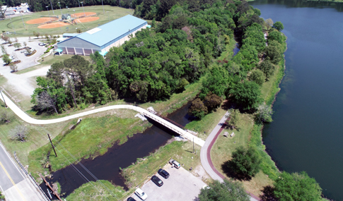 An aerial photograph shows a multi-use park trail crossing a body of water beside a small lake