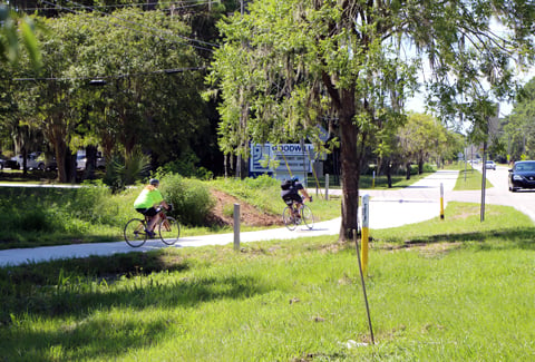 Two bicyclists wearing helmets ride on a suburban park trail.