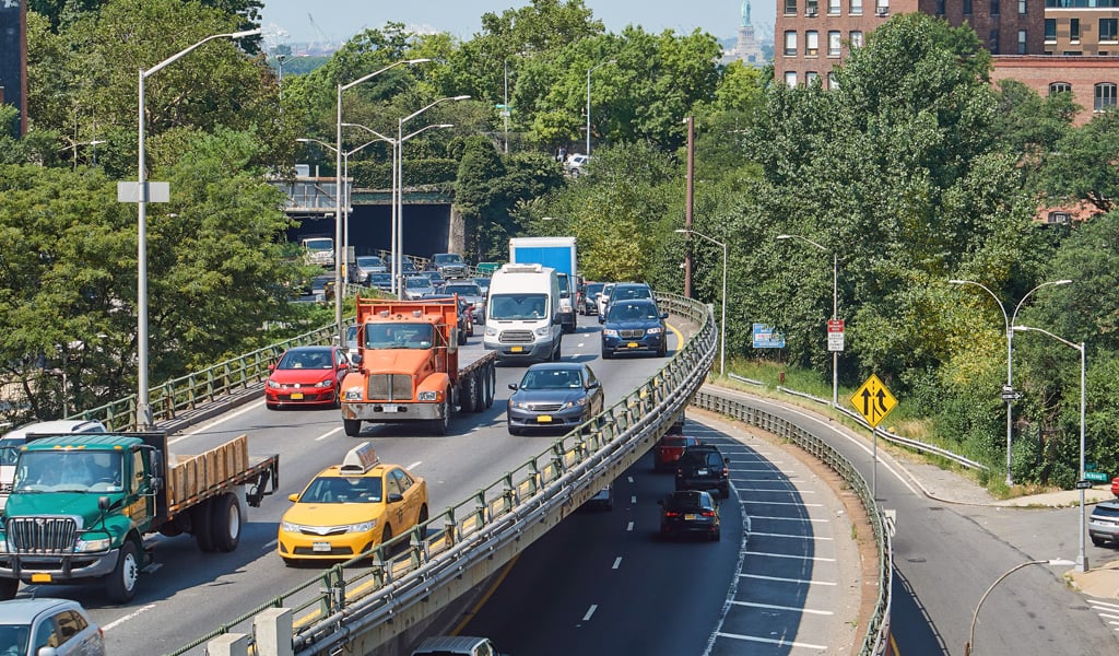 Cars and trucks driving on a highway in New York City with Statue of Liberty in the distance.