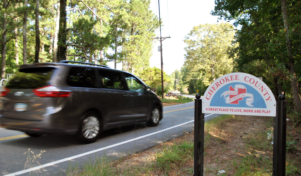 A gray minivan passes by a Cherokee County welcome sign.