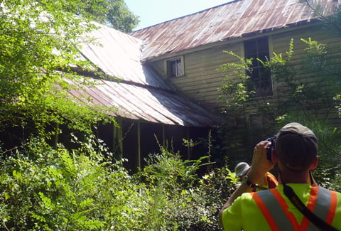 Person photographing historic home in wooded area