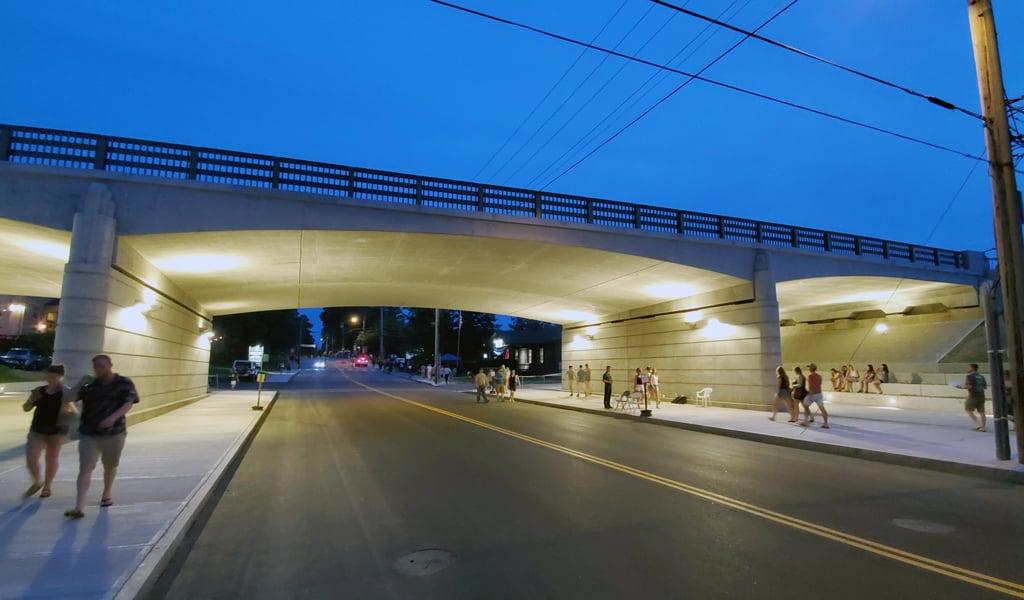 People walk under the newly reconstructed Main Street Bridge at twilight