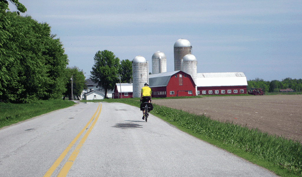 A bicyclist on a rural Vermont road near a red barn.