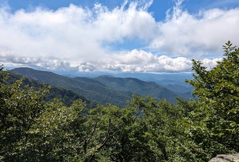 A picturesque view of Linville Falls from atop a peak overlooking a green forest.