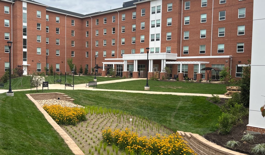 1-	Large brick student housing building with green grass and blooming bioretention basin.
