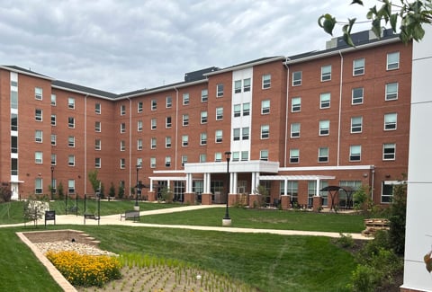 1-	Large brick student housing building with green grass and blooming bioretention basin.