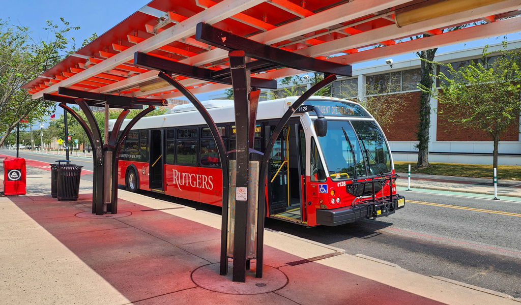 A red, white and black Rutgers bus under a red canopied bus stop.