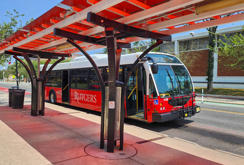 A red, white and black Rutgers bus under a red canopied bus stop.