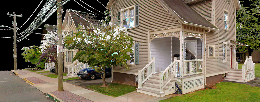 Isometric view of a detailed, cutaway digital model of a two-story house showing interior rooms and furnishings, surrounded by a small yard with a tree and sidewalk.