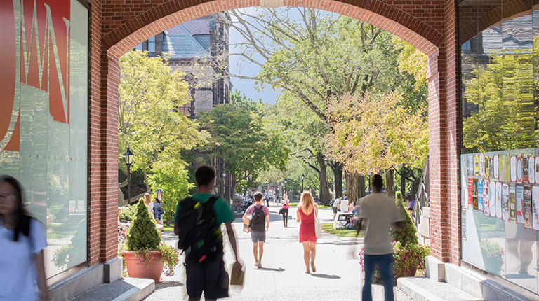 College students at Brown University walking through a pedestrian tunnel towards academic buildings on a spring day.
