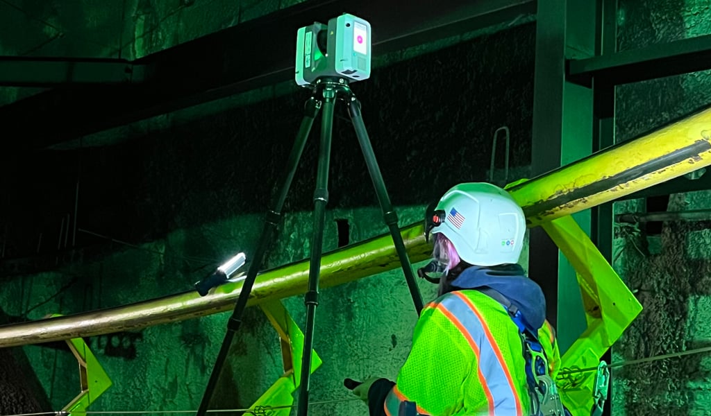 Worker in safety gear using a mounted laser to scan an indoor segment of roller coaster track.
