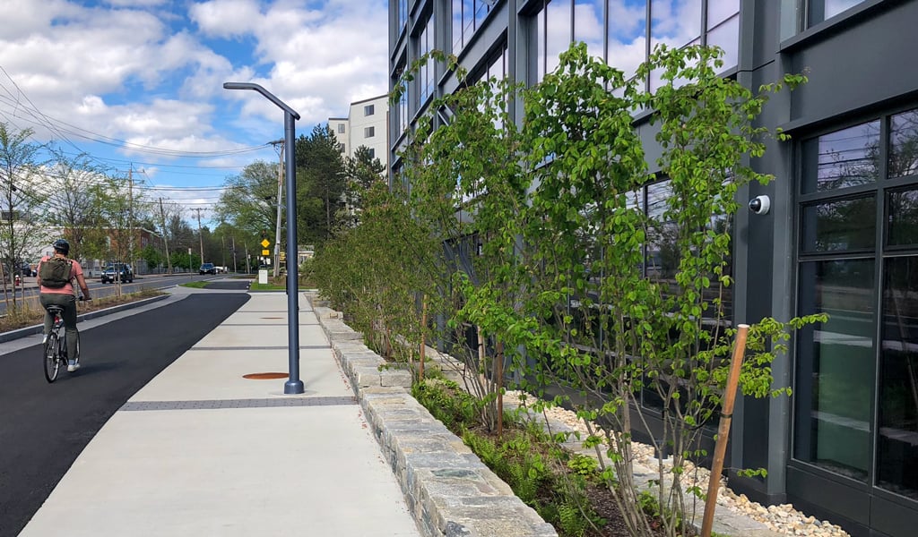 Person riding a bicycle on a paved path beside a modern glass industrial building. 