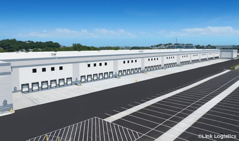 Oblique aerial of a large warehouse’s trailer drops and adjacent parking field on a sunny day with blue skies.