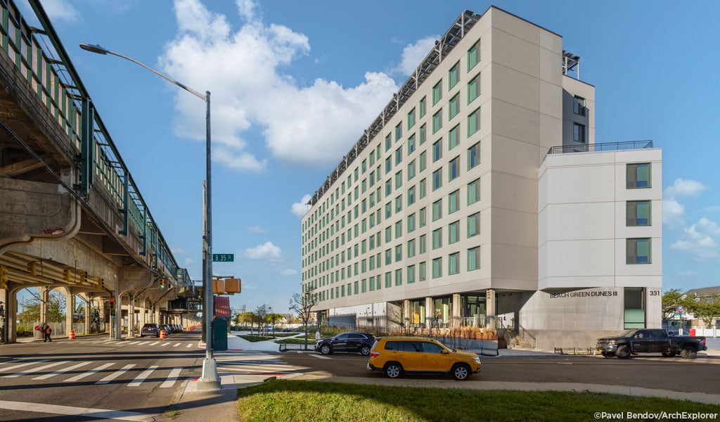 Street-level view of Beach Green Dunes III with elevated A train platform above Rockaway Freeway to the left.