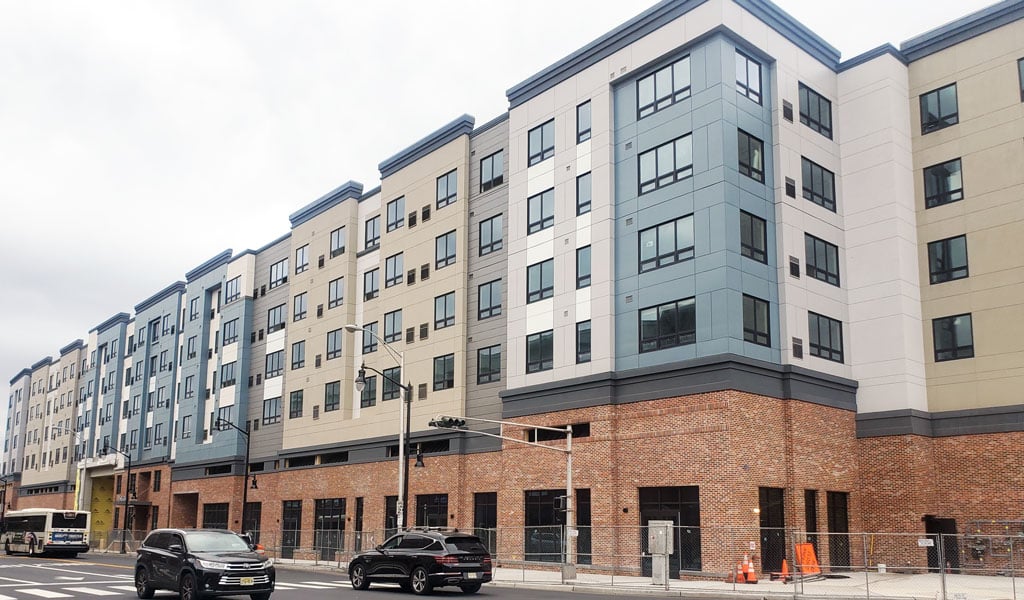 A newly constructed beige, light blue, and grey building with a brick base sits on a corner. 