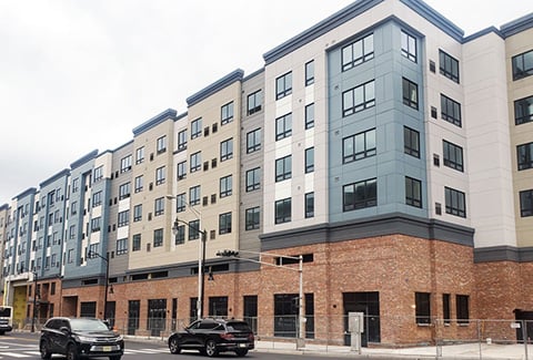 A newly constructed beige, light blue, and grey building with a brick base sits on a corner. 