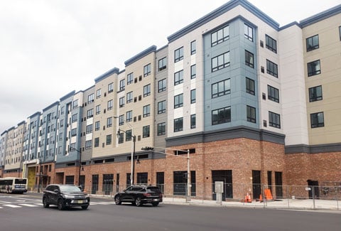 A newly constructed beige, light blue, and grey building with a brick base sits on a corner. 