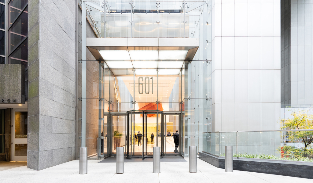 Glass entrance to a modern office building in New York City with a 601 sign above revolving doors and people inside. 