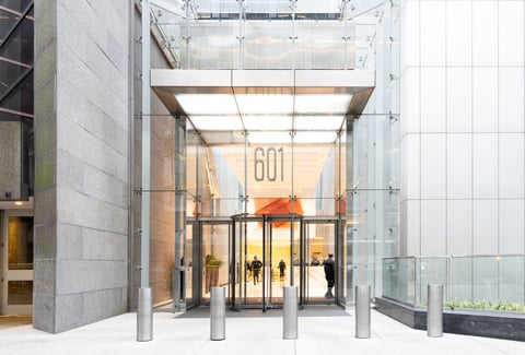 Glass entrance to a modern office building in New York City with a 601 sign above revolving doors and people inside. 