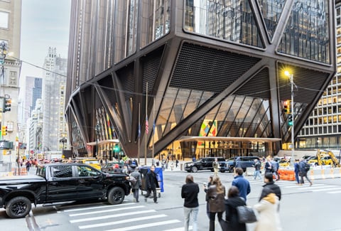 Pedestrians and vehicles at a busy city intersection in front of the JPMorgan Chase’s modern headquarters in New York City. 