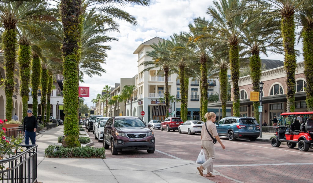 View of a pedestrian crossing the street in an upscale urban Florida shopping district lined with palm trees.