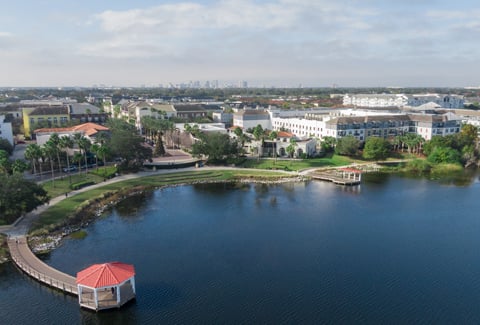 Aerial view of a lakeside boardwalk and gazebo beside a landscaped residential neighborhood with multi-story buildings.