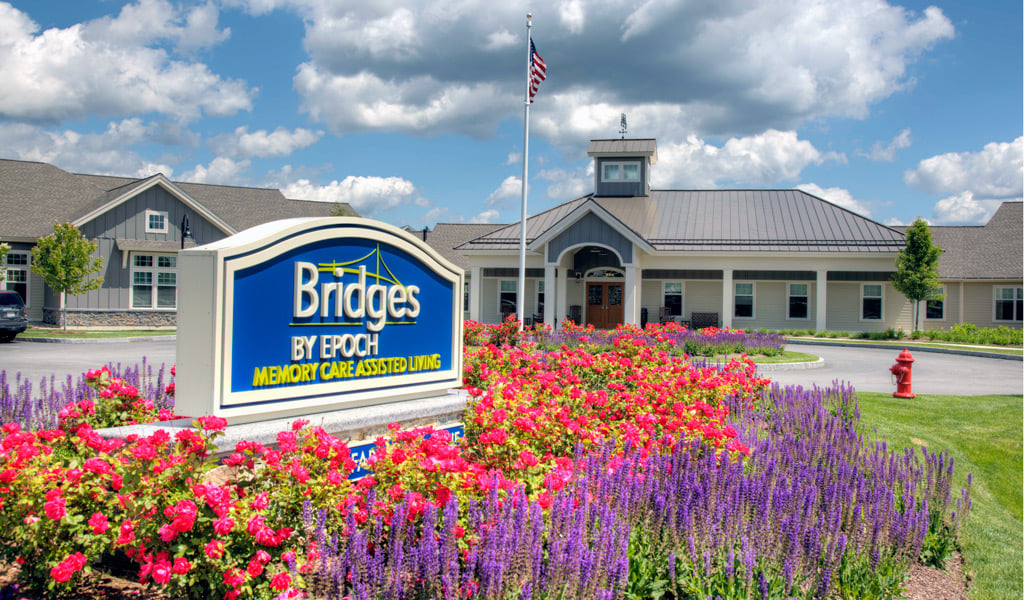 Memory care facility with colorful flower gardens in front of a modern, single-story building.